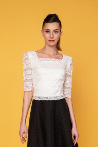 Κοντομάνικο crop top από απαλή ιβουάρ ελαστική δαντέλα, με βολάν στους ώμους και τετράγωνη λαιμόκοψη μπροστά και πίσω σε εφαρμοστή γραμμή, ιδανικό για ψηλόμεσες φούστες.